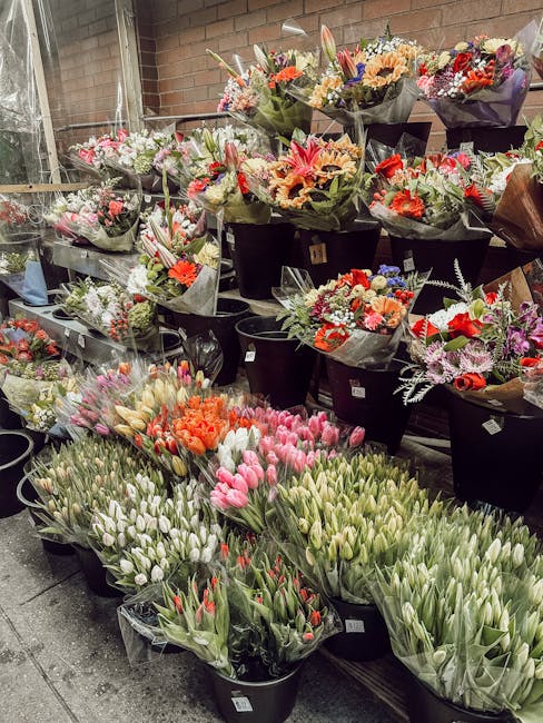 A display of freshly arranged floral bouquets and bunches in a florist shop, featuring a variety of flowers including pink tulips, orange tulips, white tulips with hints of pink, and a mix of roses, l