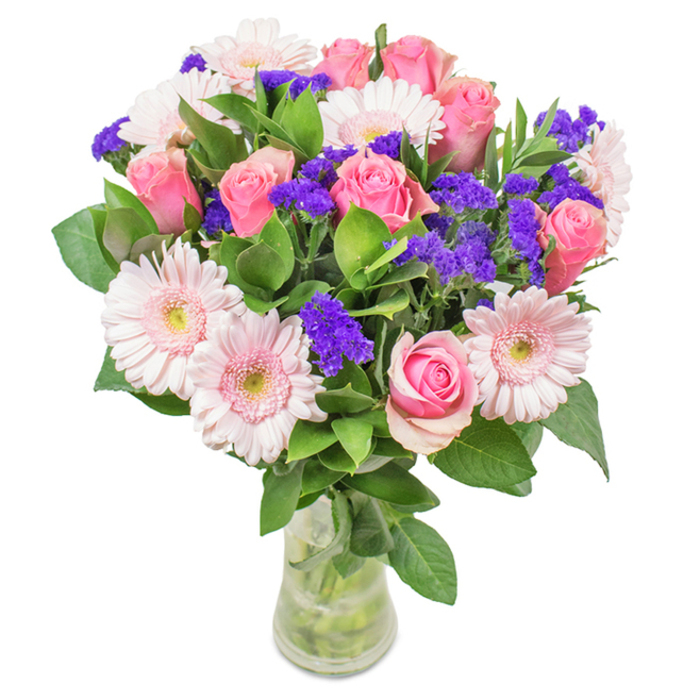 This elegantly designed bouquet from Flowers Peckham showcases a vibrant arrangement presented in a tall, clear glass vase, thoughtfully set against a crisp white background. At its heart are approximately 7-9 medium pink roses, their petals either delicately furled or just beginning to unfurl with classic spiral grace-each one a celebration of refined floral tradition. They are beautifully offset by about 5-7 soft pink gerbera daisies, their round heads and radiating petals highlighted by lighter, near-white centres that catch the natural light so characteristic of Peckham afternoons. Generous clusters of vivid purple statice, textured and striking, weave among the more subtle blooms, offering a bold contrast and a playful nod to the lively colours seen at Peckham Rye Common. Lush, deep green foliage forms an abundant base, enhancing freshness and providing a visual sense of abundance, while the clear vase-showing stems and fresh water-underscores a sense of natural vitality and local quality. This arrangement, expertly crafted for occasions from birthdays to anniversaries or simply to enliven a creative Peckham space, conveys joy, affection, and the enduring beauty of artful floristry in the heart of SE15.